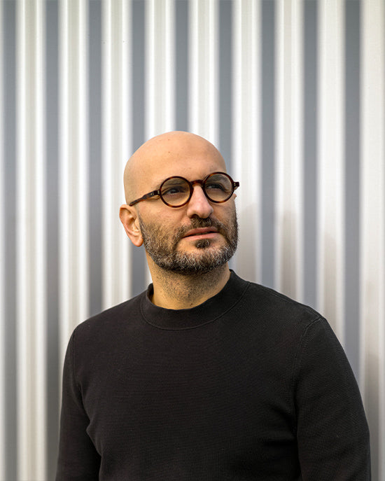 Man wearing glasses and a black sweater against a corrugated metal background