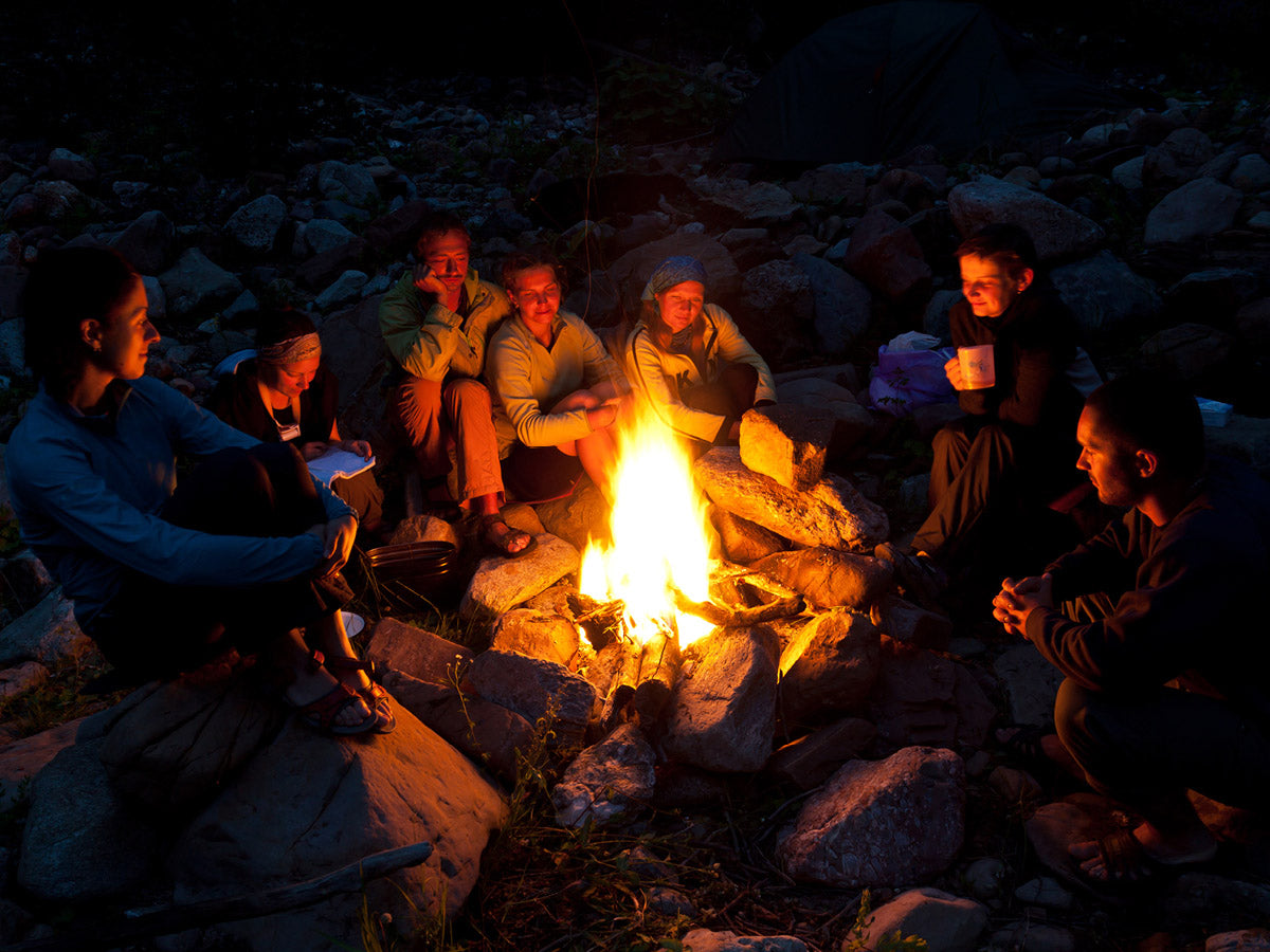Group of people sitting around a campfire at night in a rocky outdoor setting