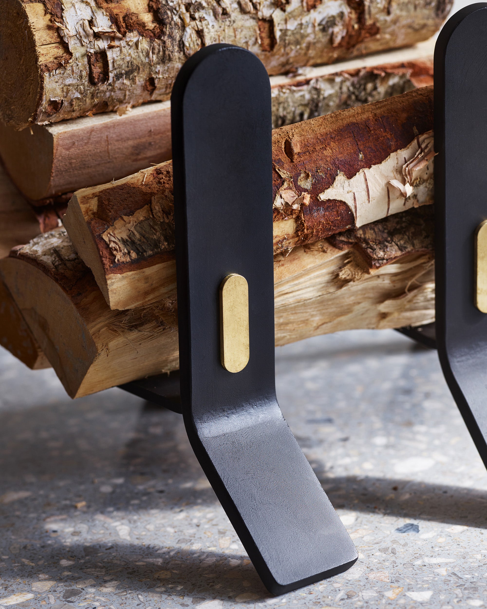 Black firewood holder with a gold accent on a background of stacked logs.