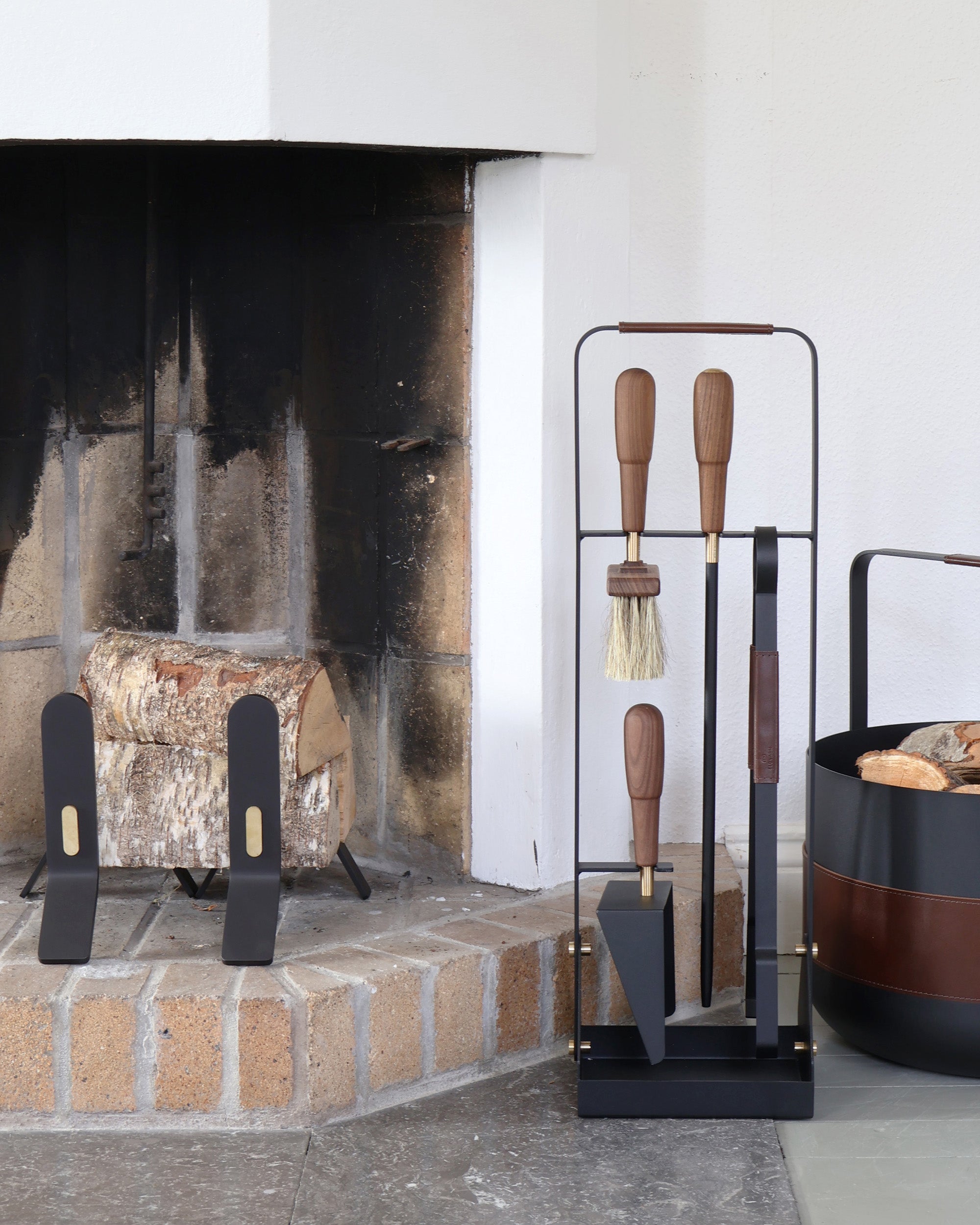 Fireplace with tools and a log, next to a stand with more tools and a fire pit.