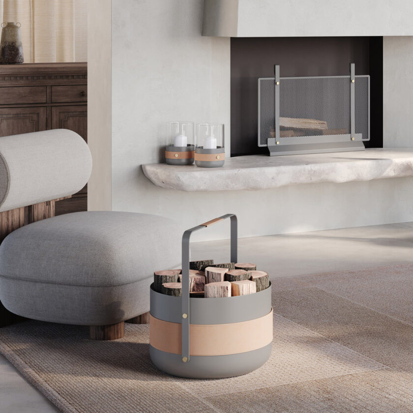 Emma Basket in Scandie (medium grey powder-coated steel, beige leather and brass details) filled with logs, in a living room with a fireplace.