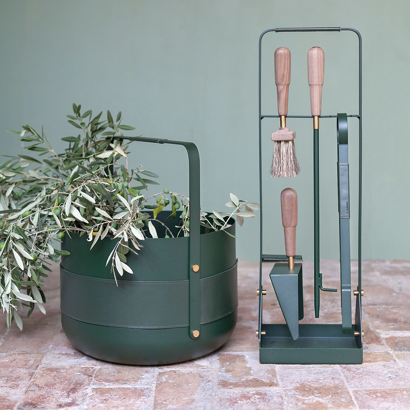 Emma Companion Set in Forêt (British racing green powder-coated steel, “Forêt” green leather, walnut wood handles and details in solid brass) outdoors with a basket in the same colour.