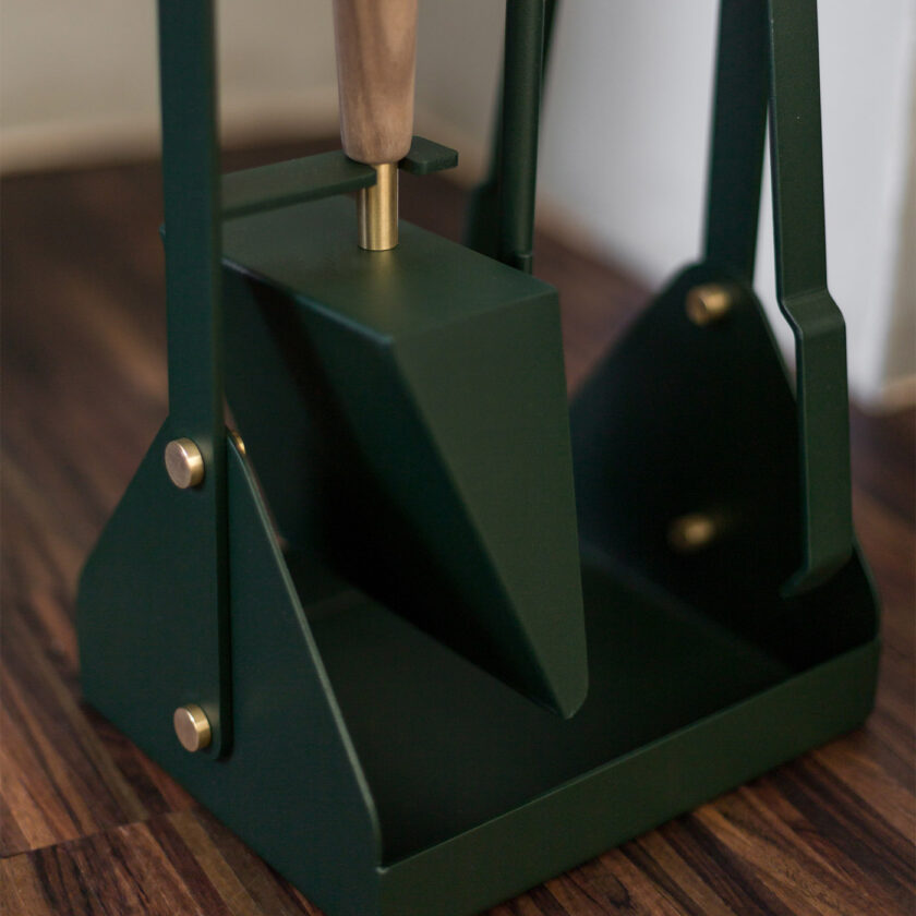 Close up of the base of Emma Companion Set in Forêt (British racing green powder-coated steel, “Forêt” green leather, walnut wood handles and details in solid brass), showing the shovel and the stand.