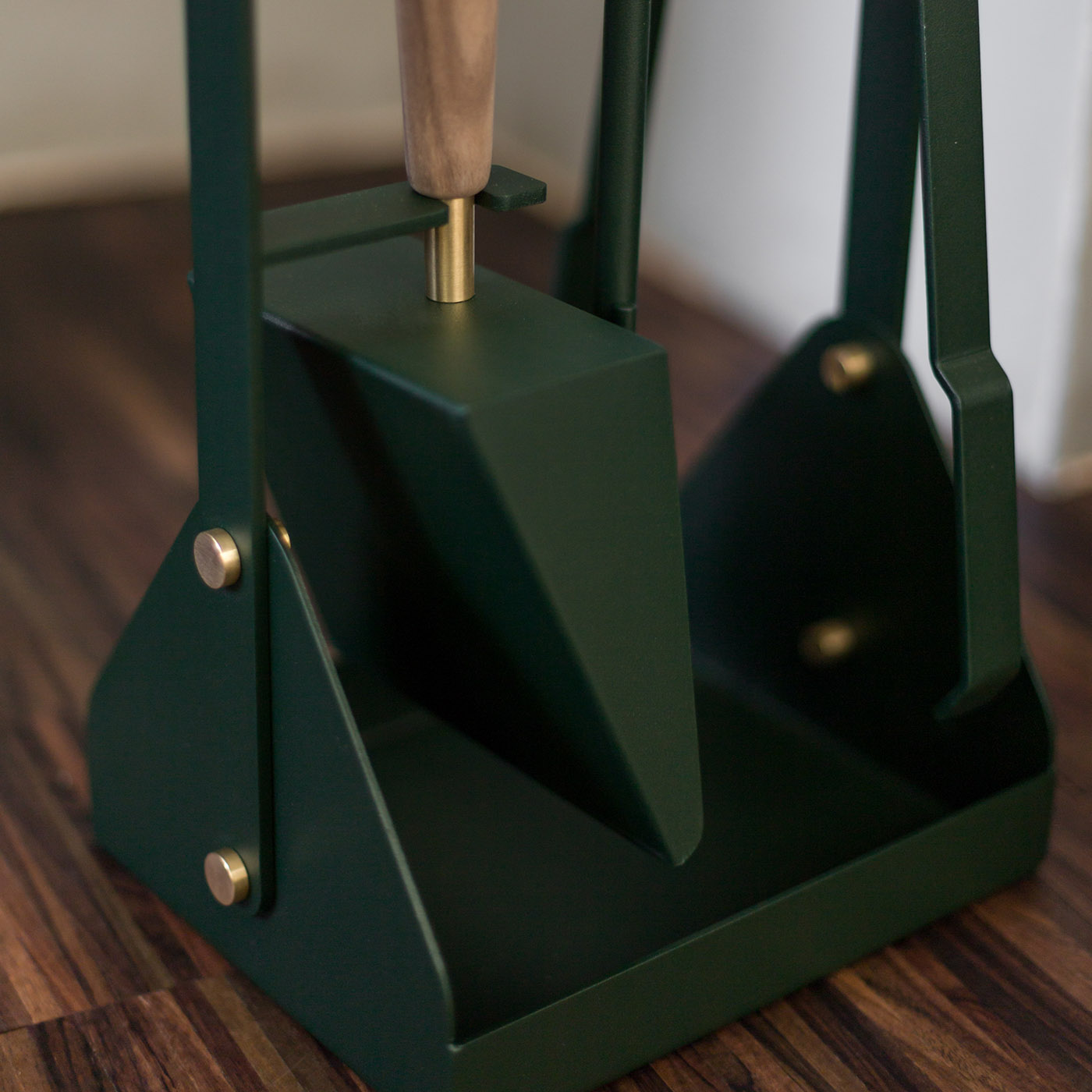 Close up of the base of Emma Companion Set in Forêt (British racing green powder-coated steel, “Forêt” green leather, walnut wood handles and details in solid brass), showing the shovel and the stand.