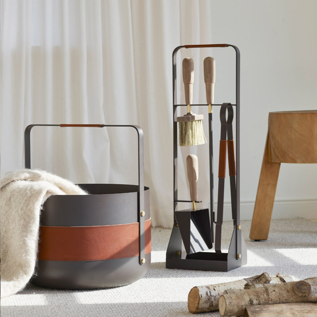 Emma Companion Set in Havane (dark warm grey powder-coated steel, “Havane” brown red leather, walnut wood handles and details in solid brass) next to a basket in the same colour.