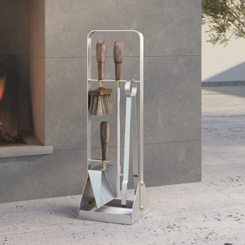 Emma Companion Set in Lumière (stainless steel, oiled walnut wood handles and details in solid brass) outdoors next to a fireplace.