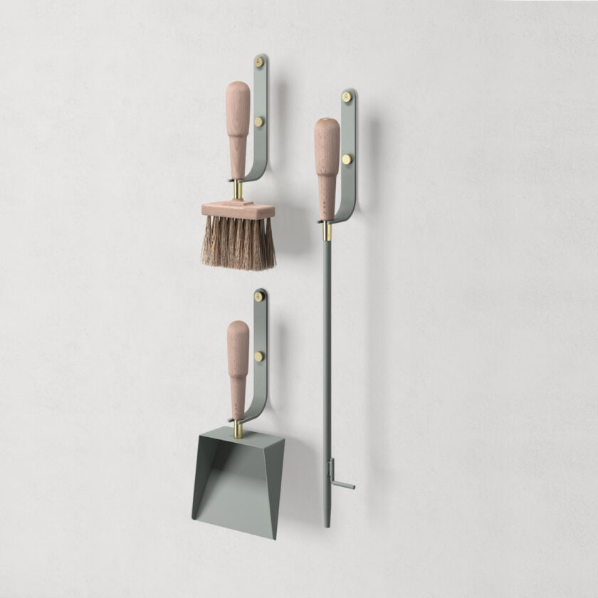 Emma Wall in Lichen (light green grey powder-coated steel, beech wood and brass details) includes 3 wall hooks, a blow poker, and a shovel and brush.