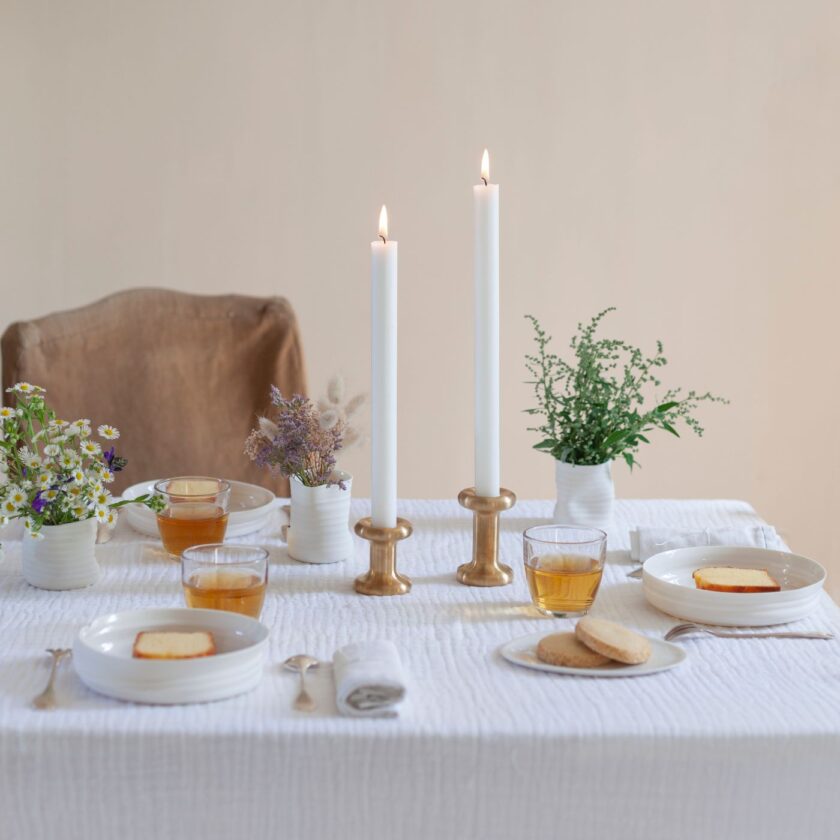 Lucie Candle Holder in two heights in solid brass, with lit candles, at table set for breakfast