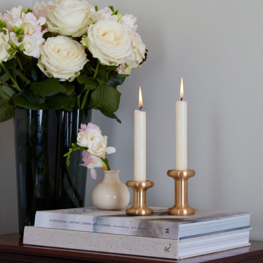 Lucie Candle Holder in solid brass, shown in two heights, on top of books.