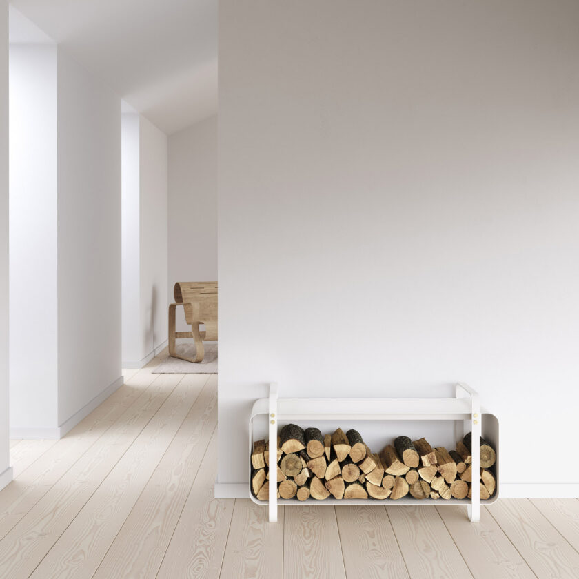 Ninne Bench in Blanc (cream white powder-coated steel with brass details) holding wood inside of it in a white room.