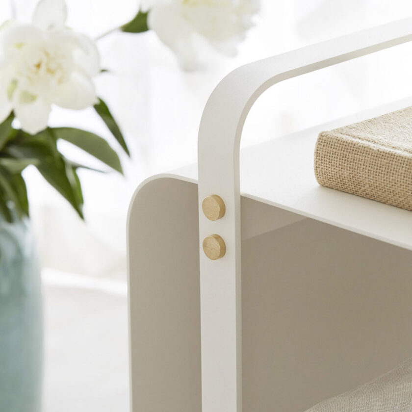Close up of Ninne Bench in Blanc (cream white powder-coated steel and brass details) next to white flowers.