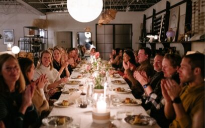 Image of the Hygge life dinner with many people sat along a table clapping.
