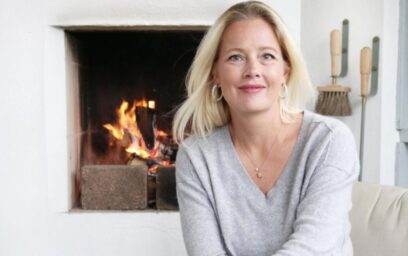 Louise Varre smiling next to a lit fire and the Emma Wall Set in Lichen.