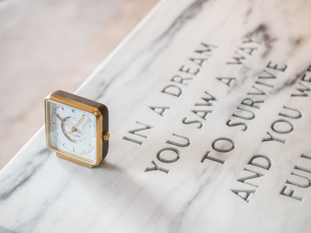 The Eldvarm x Båge and Söner clock made of white, grey and gold-plated stainless steel placed on marble.