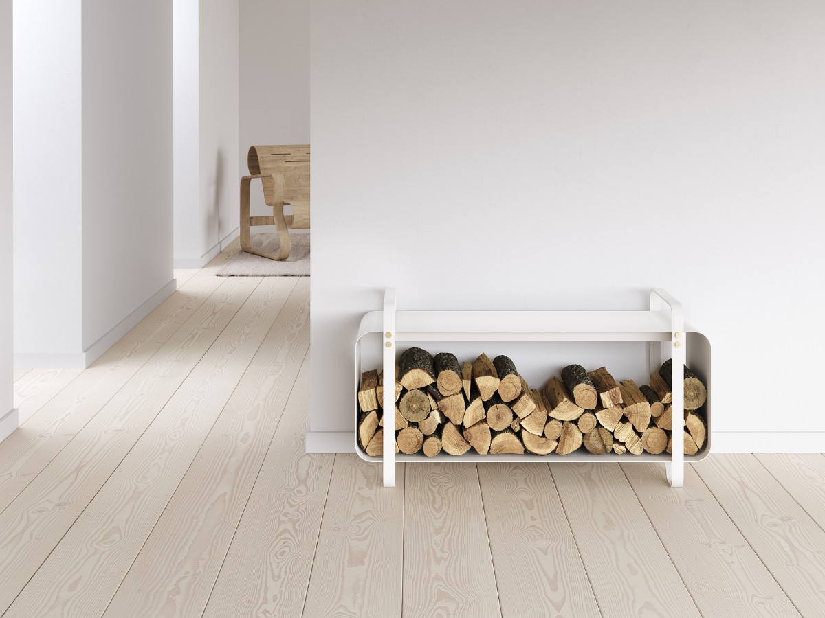 Ninne Bench Blanc (cream white powder-coated steel with details in solid brass) in a white room with wood stacked in it.