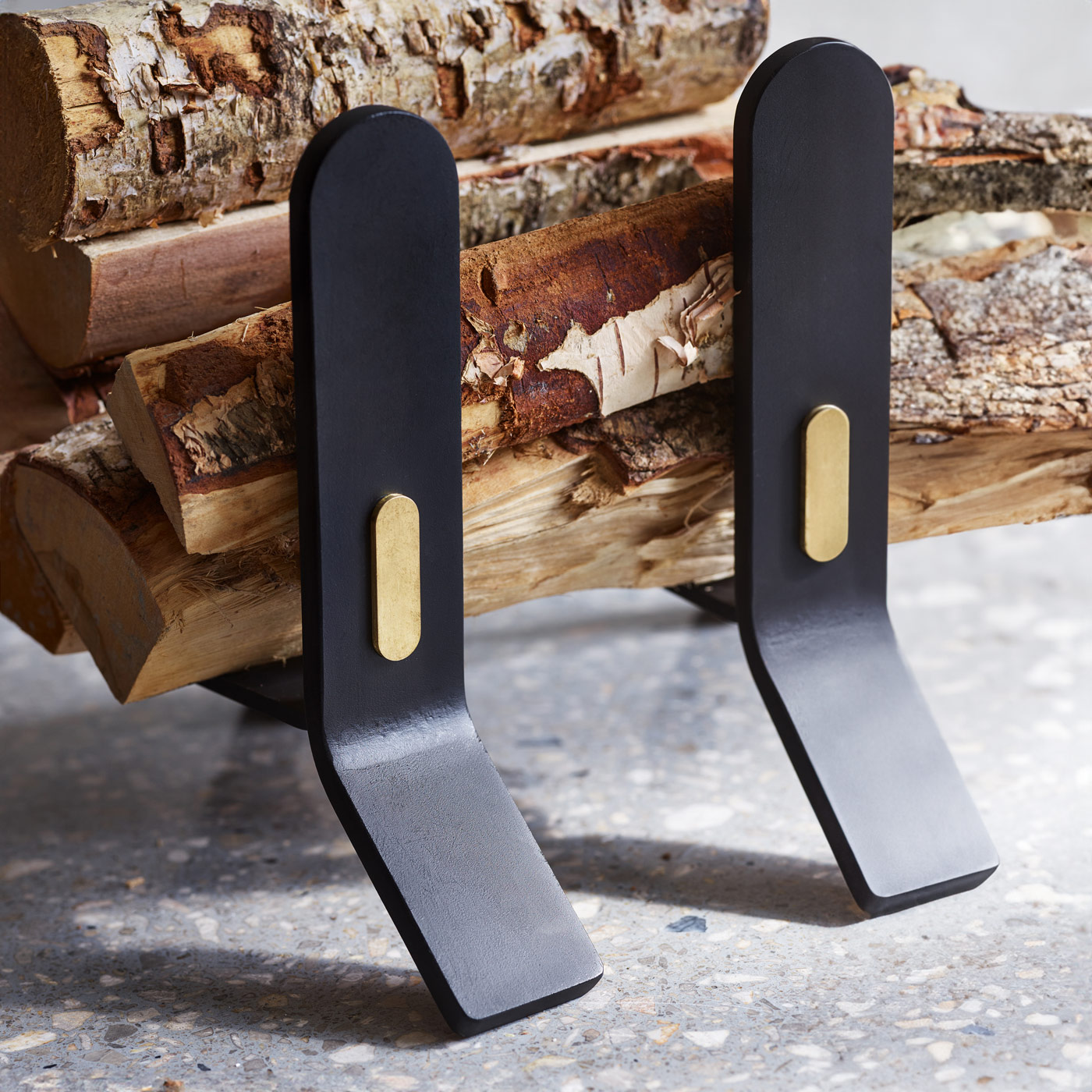 Close up of Cooper Fire dogs in noir with brass details with wood on top of it.