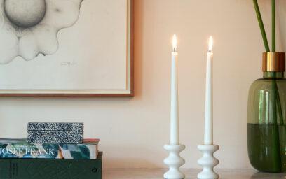 A pair of LouLou Candle holders in Blanc (white) on a mantlepiece next to books and flowers.