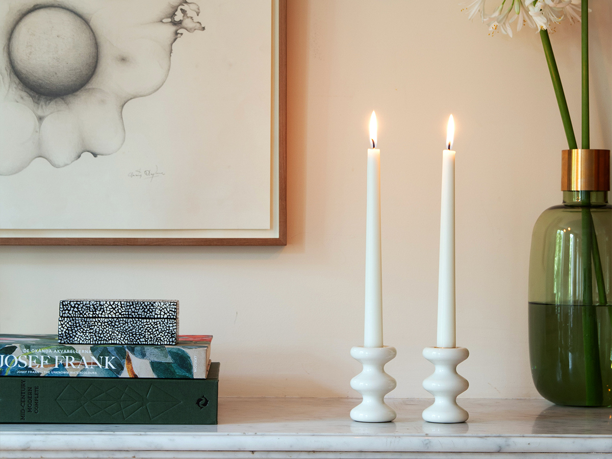 A pair of LouLou Candle holders in Blanc (white) on a mantlepiece next to books and flowers.