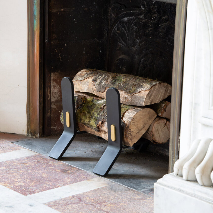 The Cooper Fire Dogs sitting in a white marble fireplace. The Noir version are shown here with fire wood on top of them.