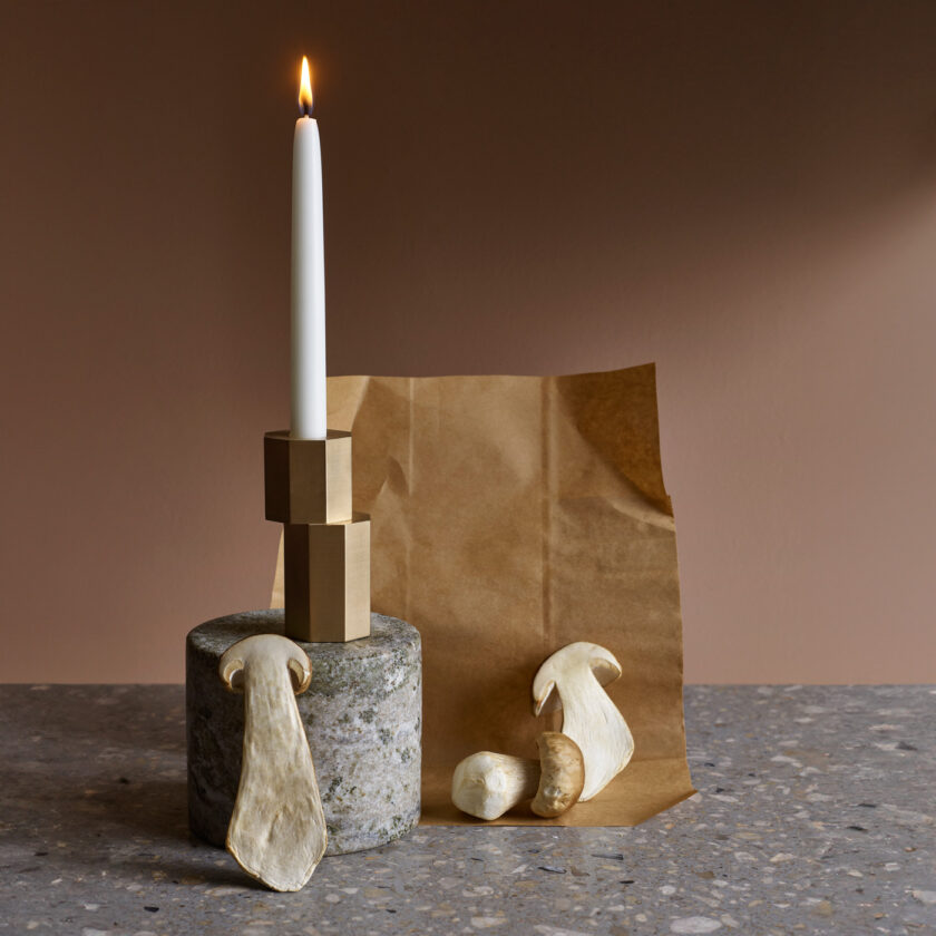 A Luca Candle Holder in solid Brass with a lit candle.