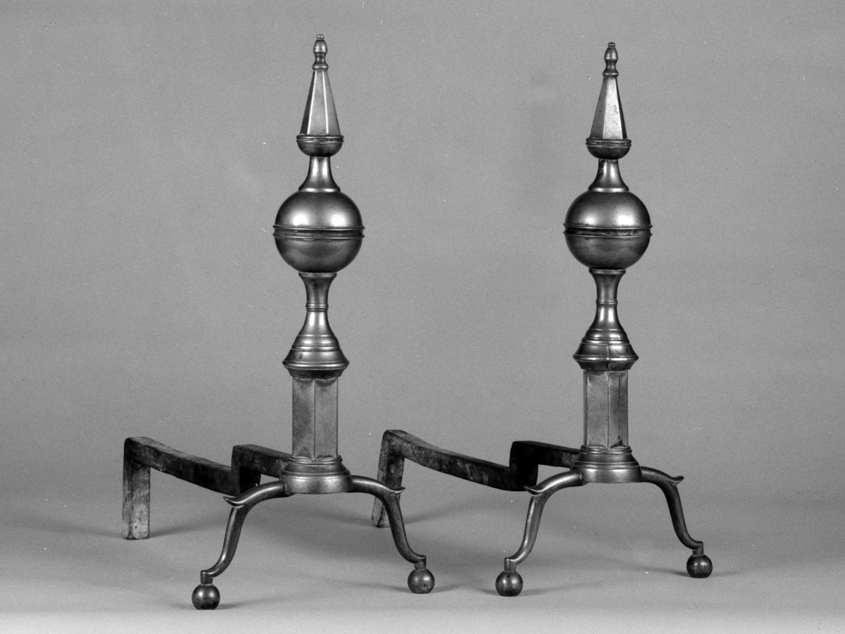 A pair of dark brass antique andirons circa 1800. Made in the USA, these pieces are now part of the American art collection at the The Metropolitan Museum of Art.