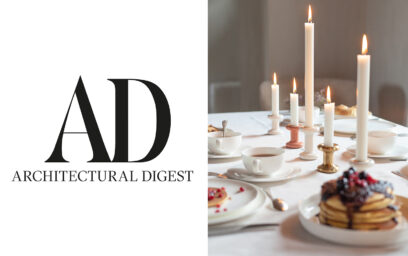 The Architectrual Digest logo, beside a photo of the Lucie Candle holders on a breakfast table. Featured are the small and large Lucie Candle Holders in Brass, Blanc and Bonbon.