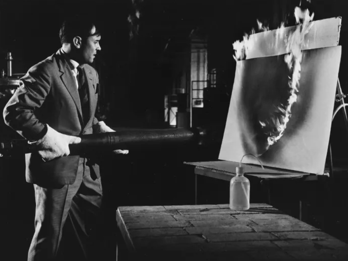 A black and white photo of Artist Yves Klein using creating art with fire.