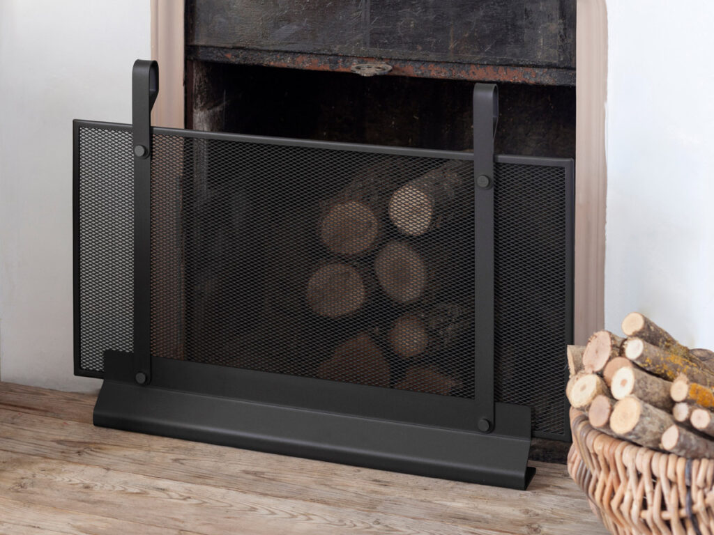 An Emma Firescreen Small in Noir in front of an fireplace with firewood in it.