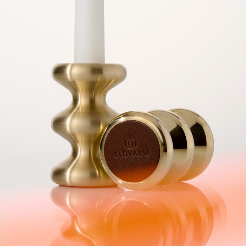 A brushed brass LouLou Candle Holder standing beside a polished brass LouLou Candle Holder on it side showing the leather pas on the bottom of our candle holders.