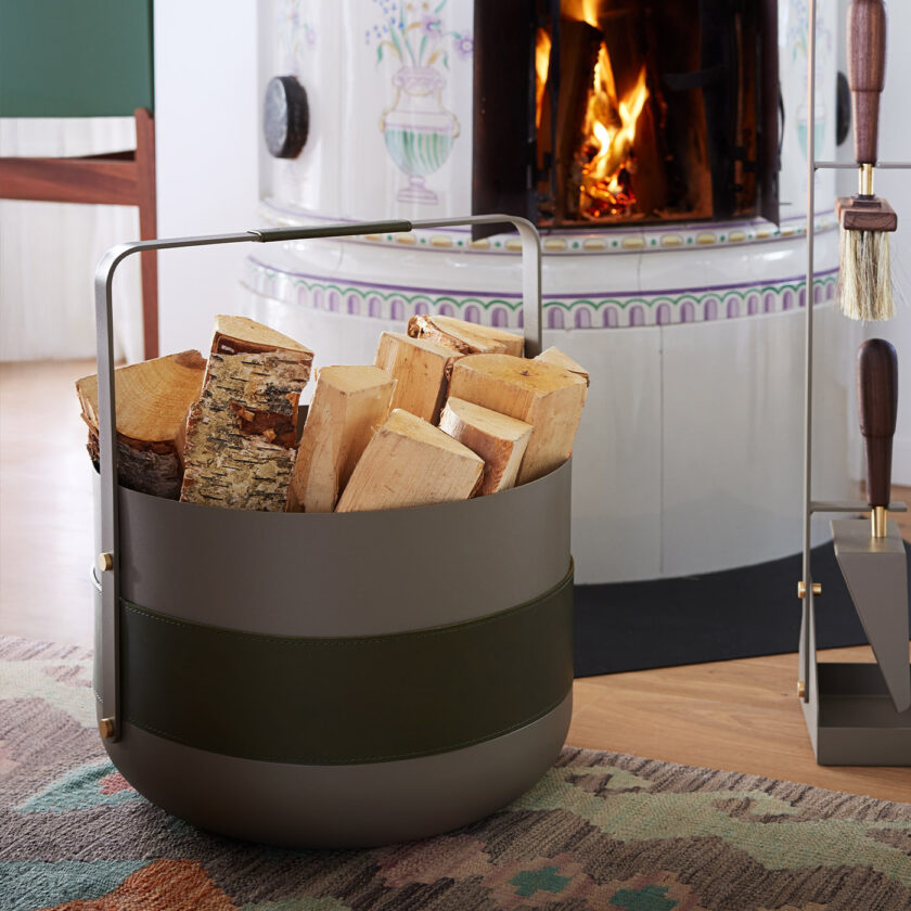 The Emma Basket in Olive full of firewood sitting in front of a white fireplace.