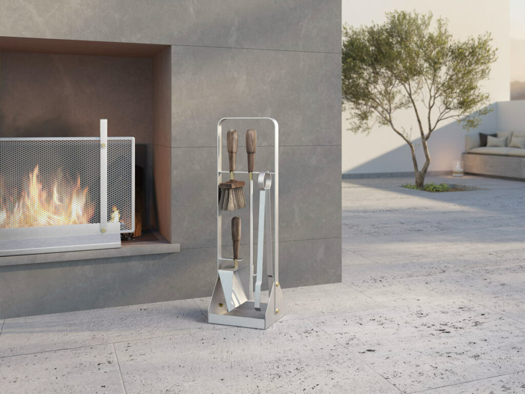 Emma Companion Set of fireplace tools in stainless steel, next to a screen in stainless steel, in an outdoor setting